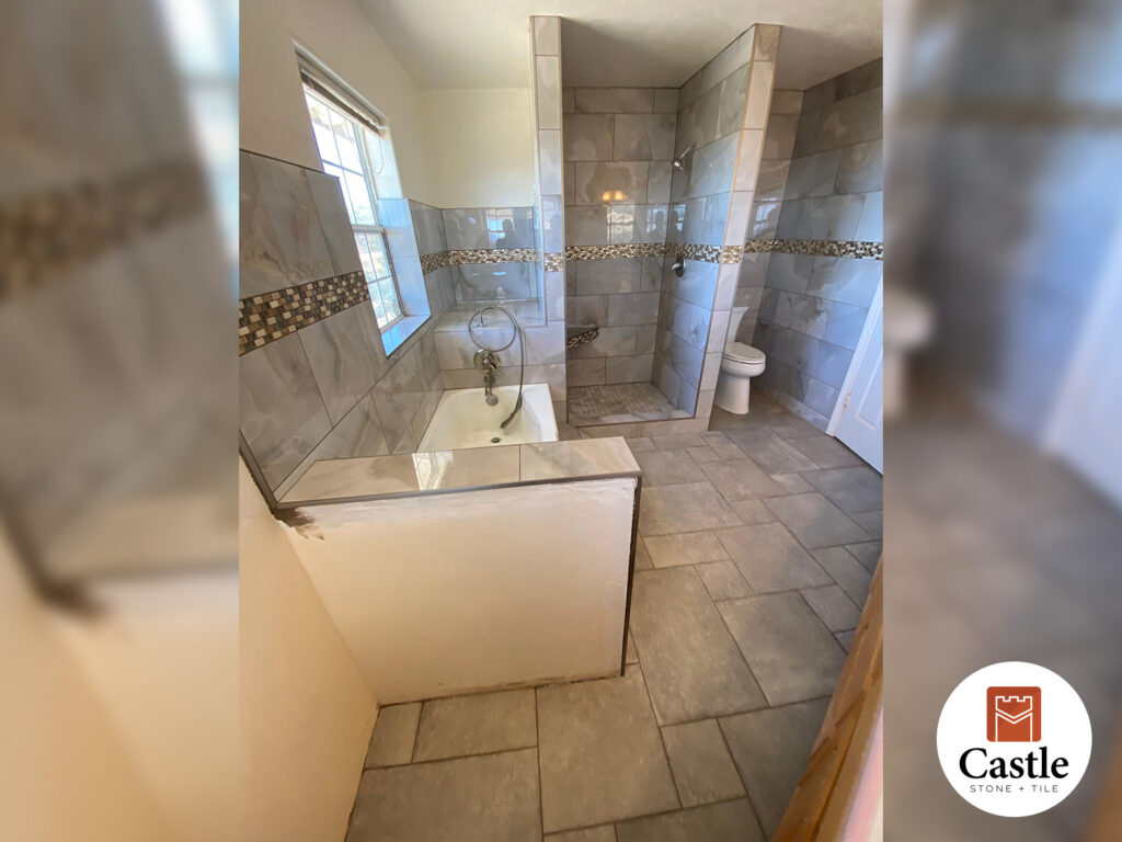 This Jamul bathroom features 12x24 earthy porcelain tiles accented by a striking gold mosaic band. A Versailles floor pattern adds timeless style and character to the space.