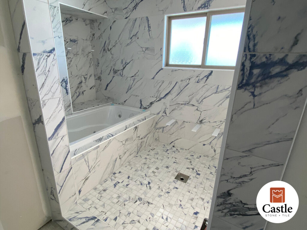 This Jamul, CA remodel features a big walk-in shower and jetted tub finished in 12x24 porcelain tile. The marble-look design creates a seamless, spa-like retreat.